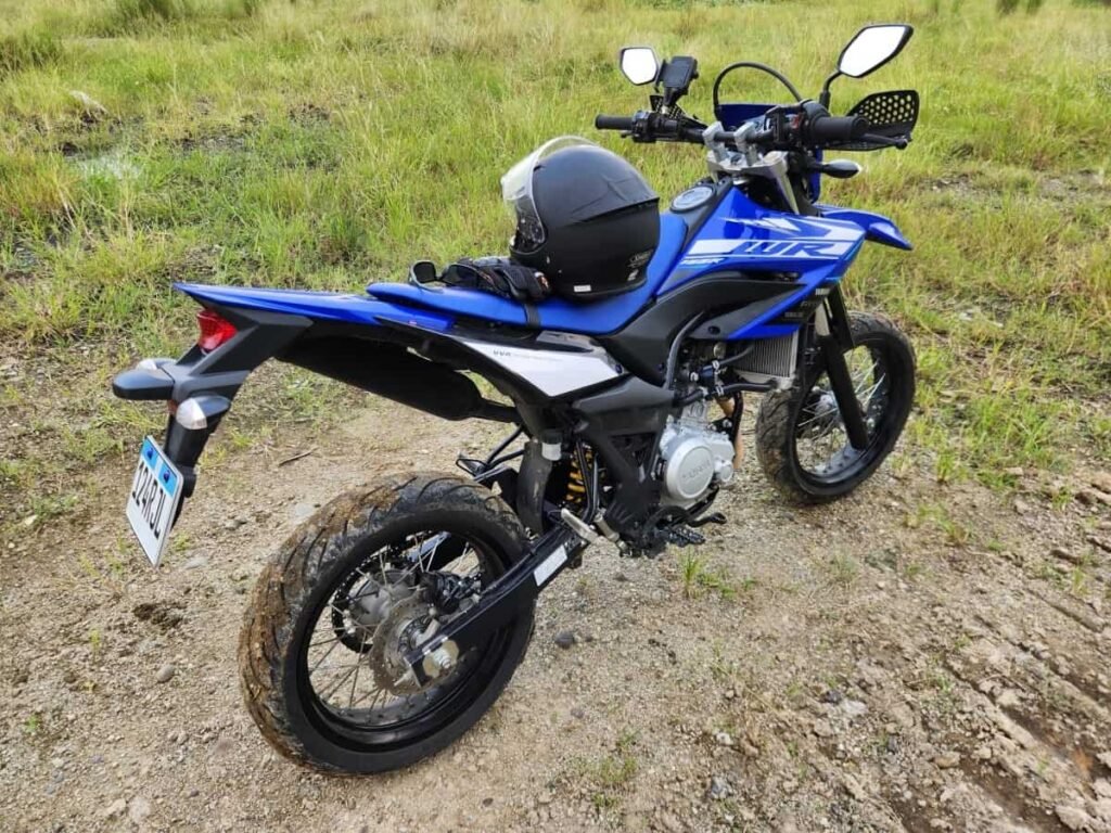 Blue Yamaha WR155R dual-sport motorcycle with a helmet on the seat, parked on a gravel trail